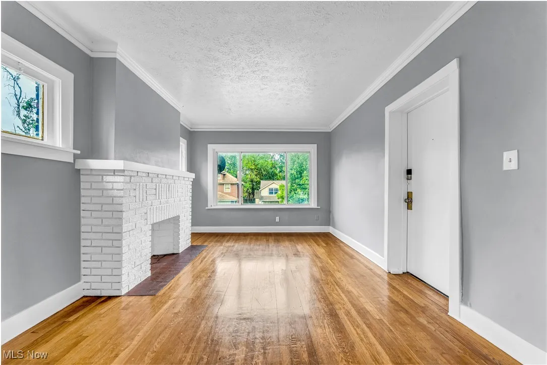 Unfurnished living room featuring a textured ceiling, crown molding, wood-type flooring, and a brick fireplace