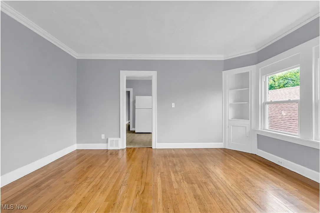 Empty room featuring light wood-type flooring, ornamental molding, and built in features
