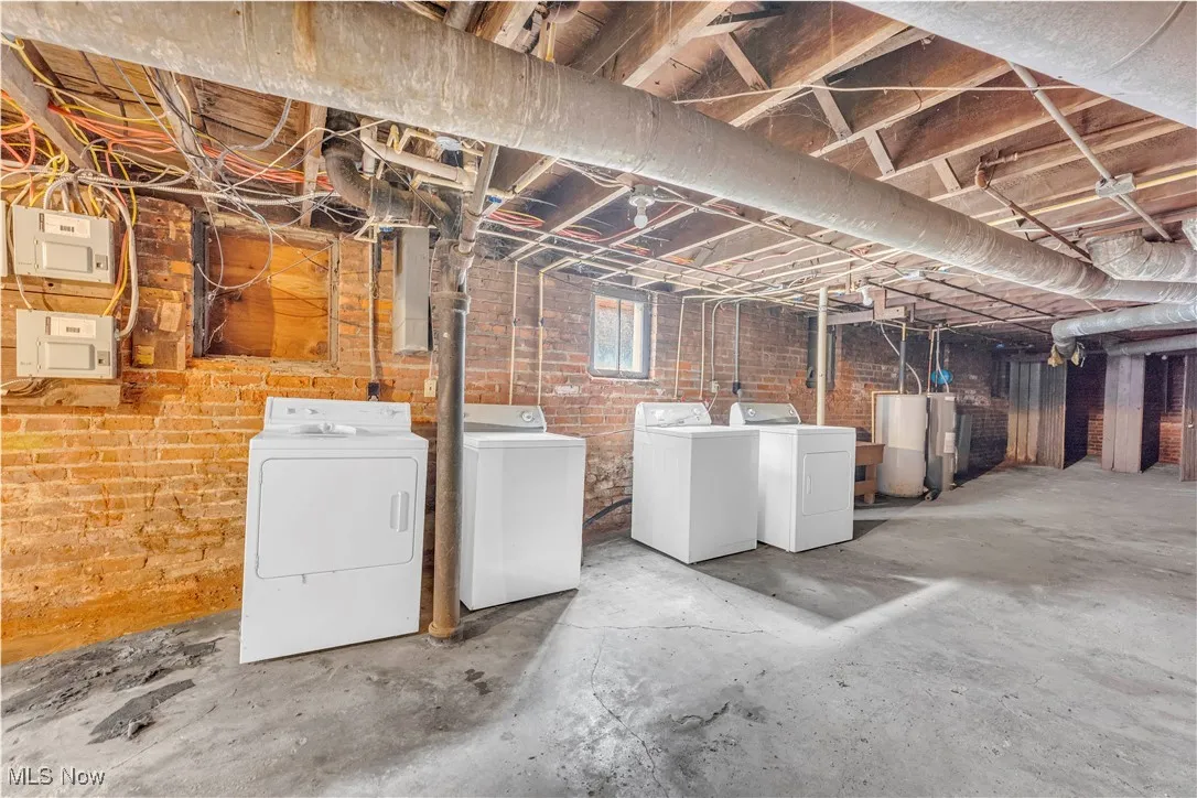 Basement with washer and clothes dryer, brick wall, water heater, and electric panel