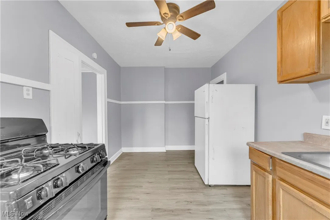 Kitchen with black range with gas stovetop, freestanding refrigerator, ceiling fan, light wood-style floors, and light countertops