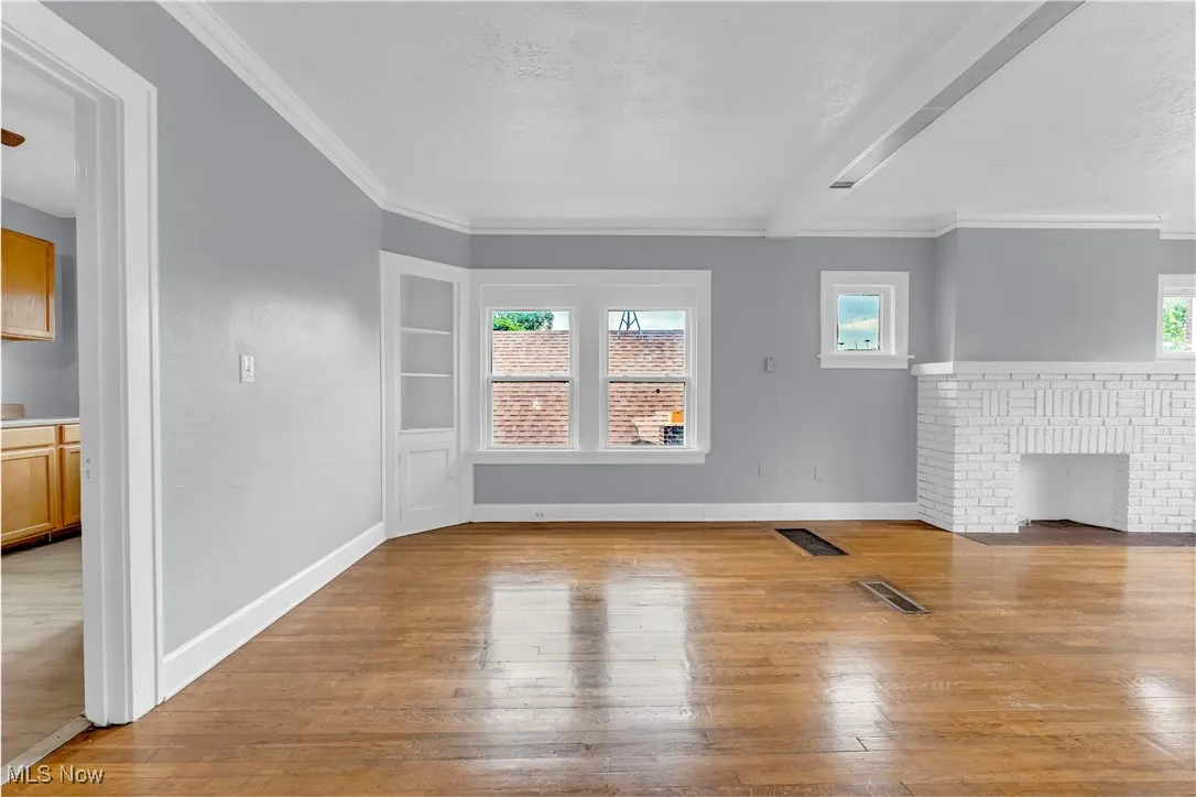 Unfurnished living room with healthy amount of natural light, ornamental molding, and wood-type flooring