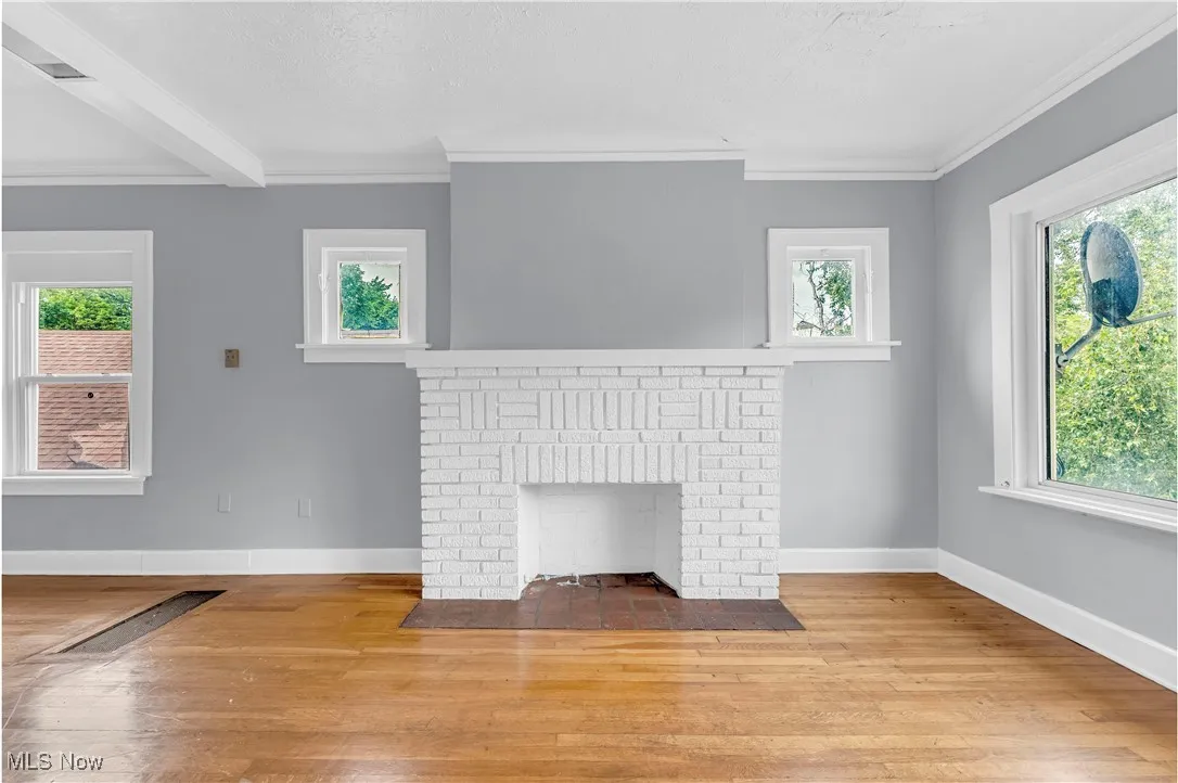 Unfurnished living room with wood-type flooring, crown molding, and a brick fireplace