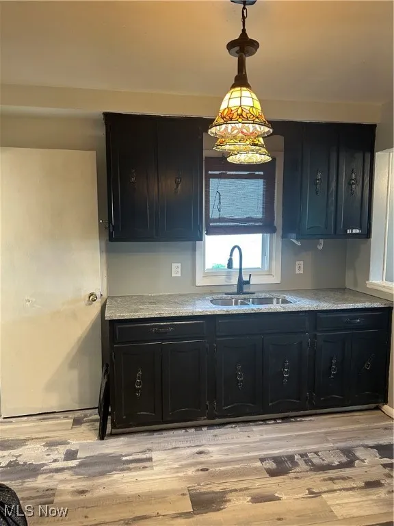 Kitchen featuring dark cabinetry, light wood-style floors, and pendant lighting
