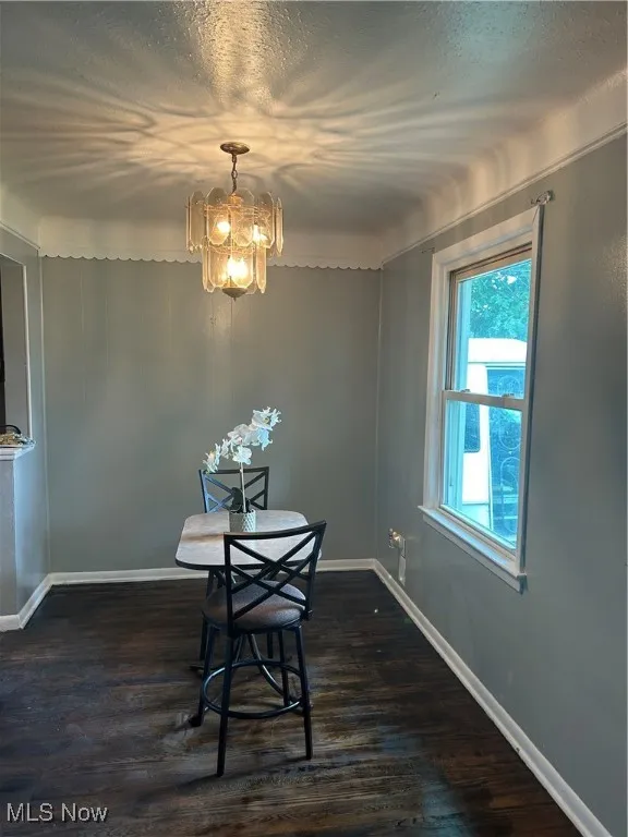 Dining space with a textured ceiling, dark wood-type flooring, and a chandelier