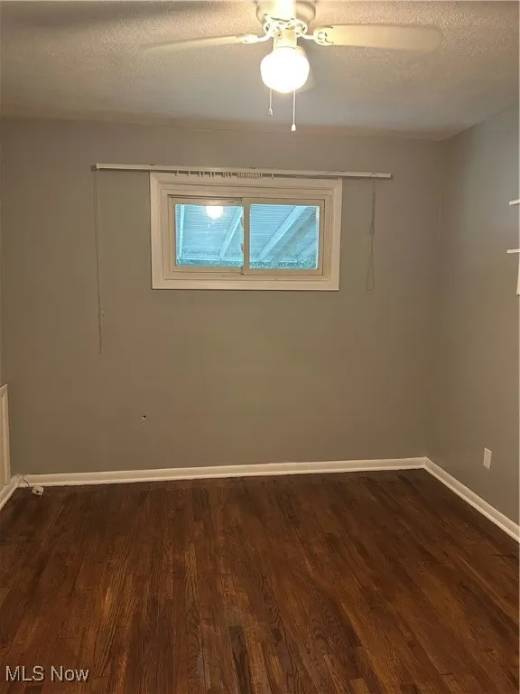Unfurnished room with a textured ceiling, dark wood finished floors, and ceiling fan