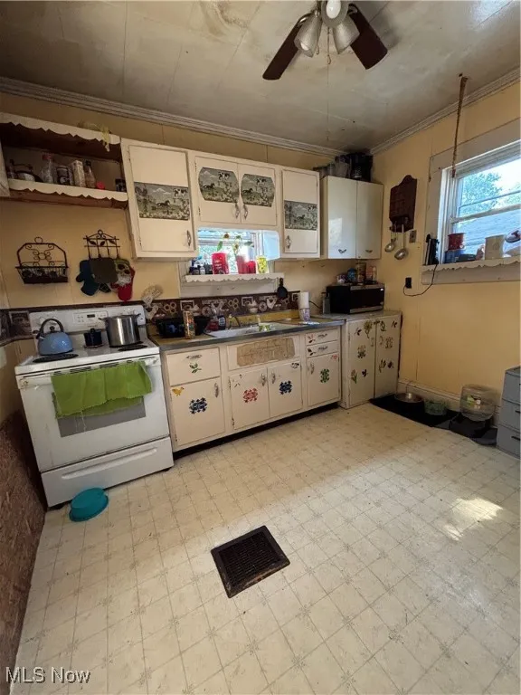 Kitchen with light floors, range, healthy amount of natural light, ornamental molding, and a ceiling fan