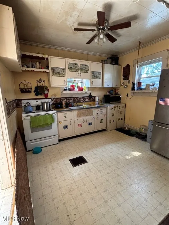 Kitchen with light floors, range, fridge, crown molding, and a ceiling fan