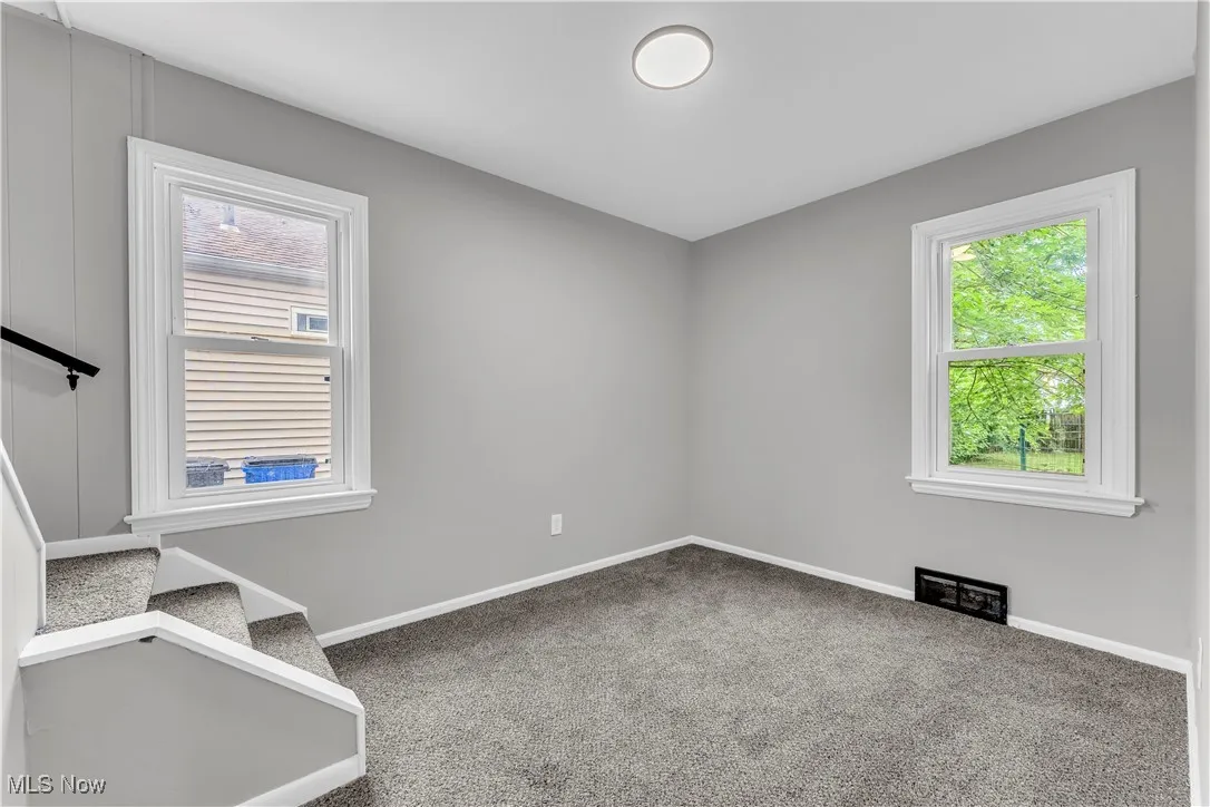 Carpeted empty room featuring baseboards and stairway