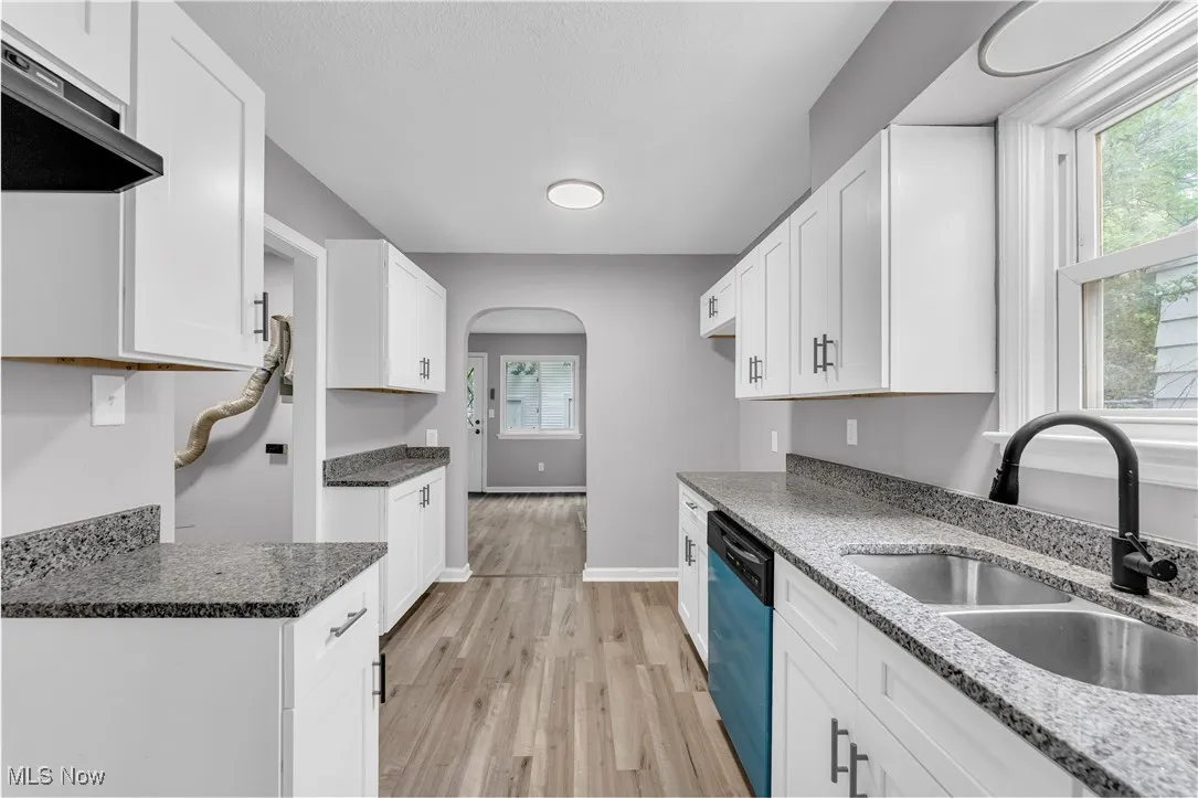 Kitchen featuring light wood-type flooring, arched walkways, white cabinetry, dishwasher, and extractor fan