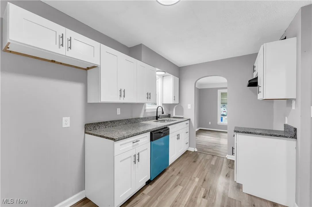 Kitchen with arched walkways, dark countertops, light wood finished floors, and white cabinets