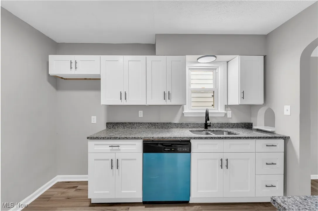 Kitchen featuring dishwasher, white cabinets, arched walkways, wood finished floors, and a textured ceiling
