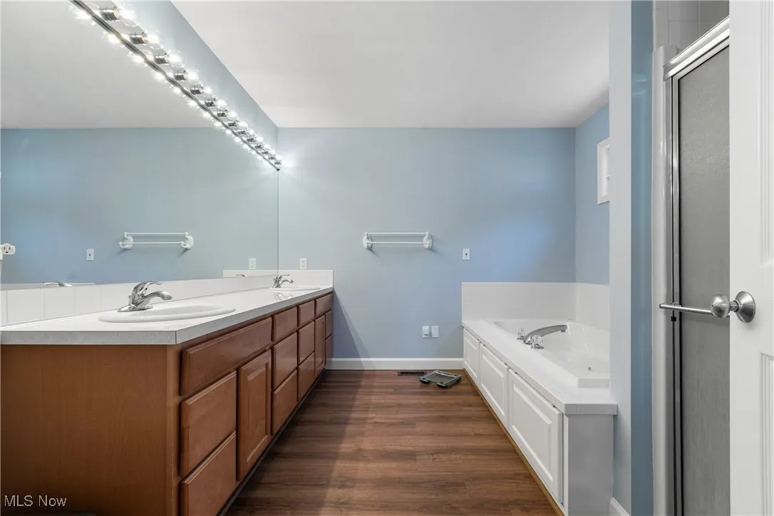 Bathroom featuring double vanity, a garden tub, and wood finished floors