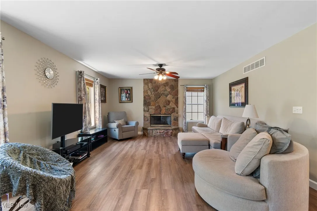 Living room featuring wood finished floors, a ceiling fan, and a stone fireplace
