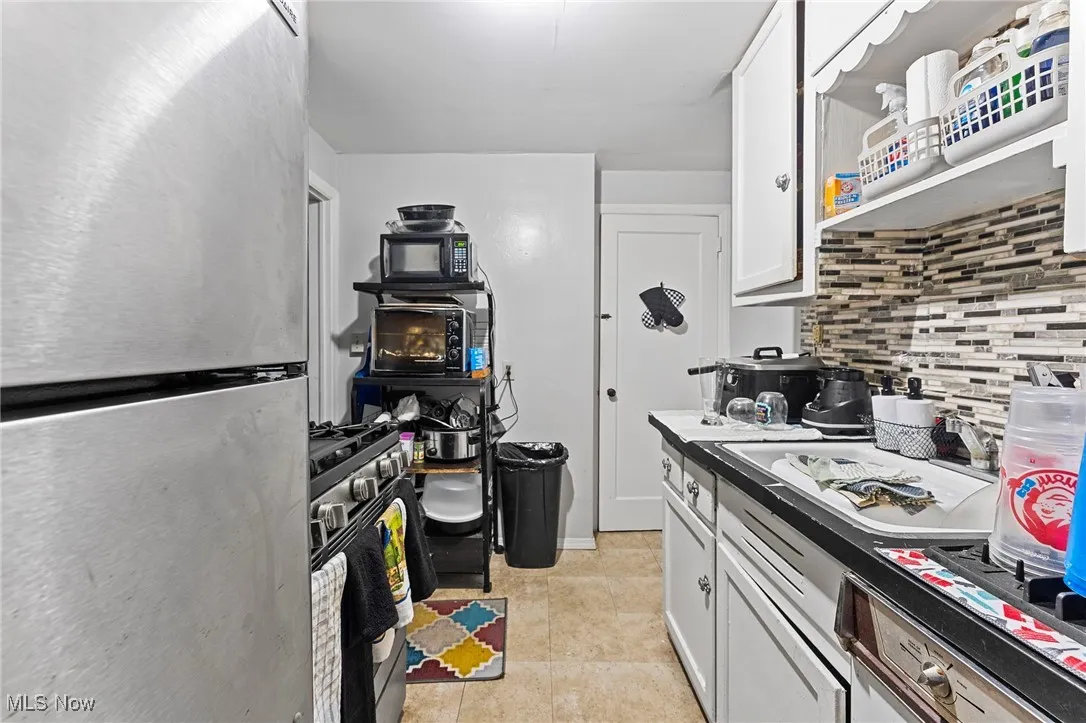 Kitchen with stainless steel appliances, decorative backsplash, white cabinetry, and light tile patterned floors