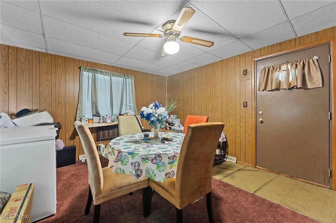 Carpeted dining space with ceiling fan, a paneled ceiling, washer / dryer, and wood walls