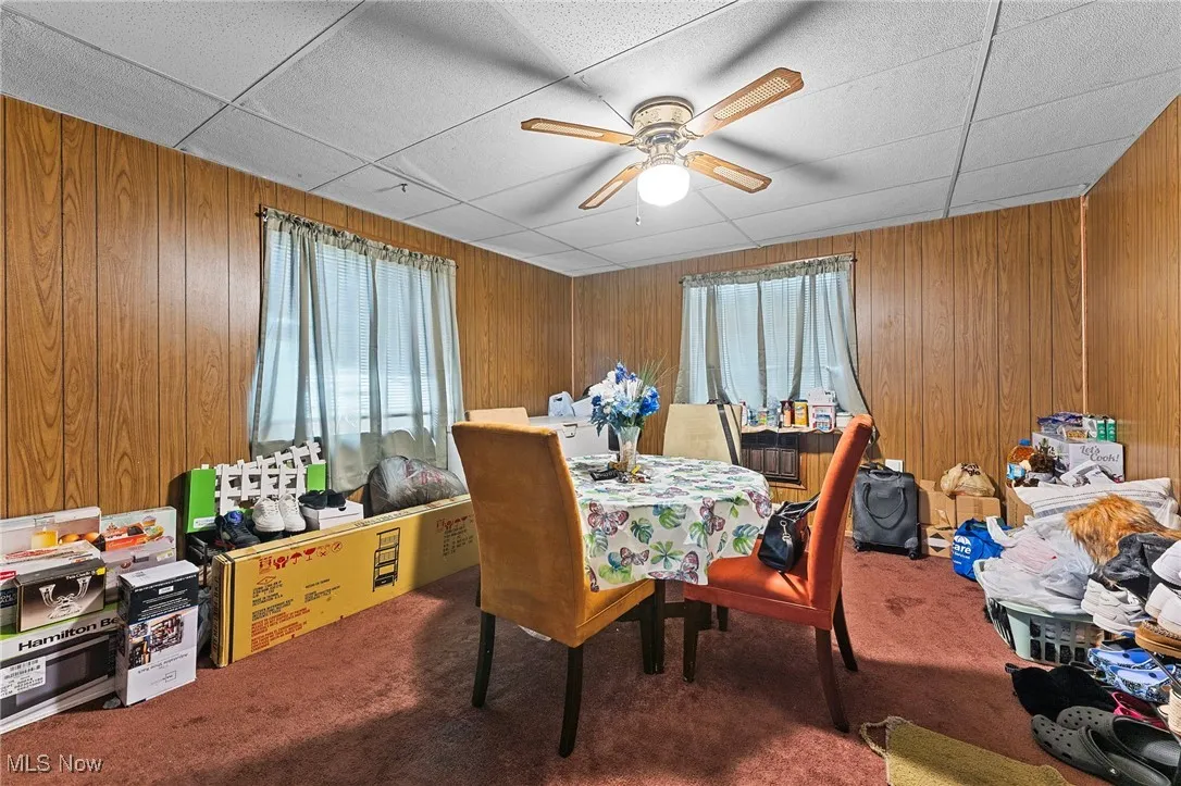 Carpeted dining room with ceiling fan, wooden walls, and a paneled ceiling