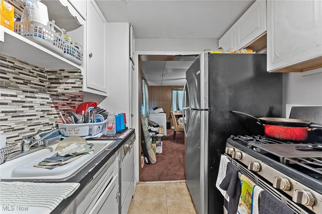 Kitchen with stainless steel gas range, white cabinets, light tile patterned flooring, decorative backsplash, and washer / clothes dryer