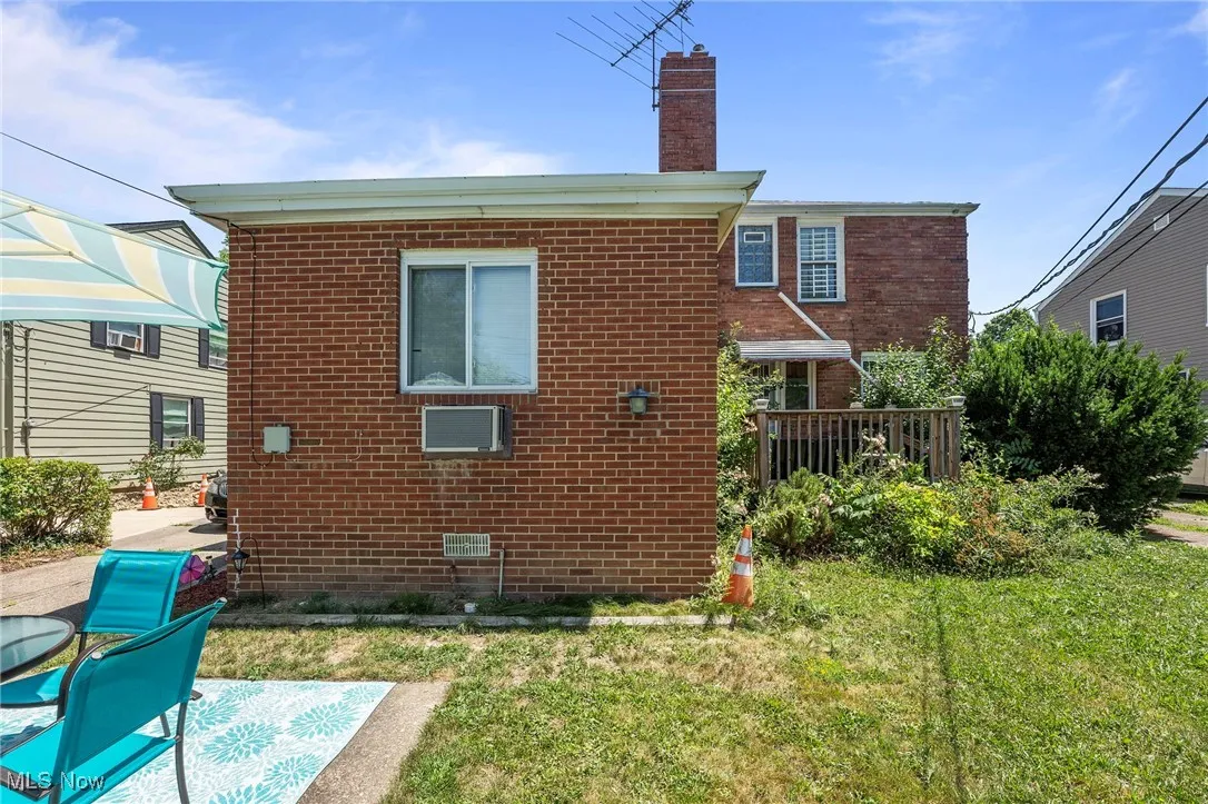 Rear view of house featuring brick siding, a chimney, and a lawn