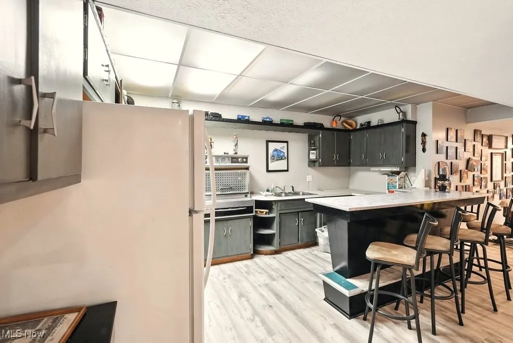 Kitchen with light wood-style flooring, freestanding refrigerator, light countertops, a peninsula, and a breakfast bar