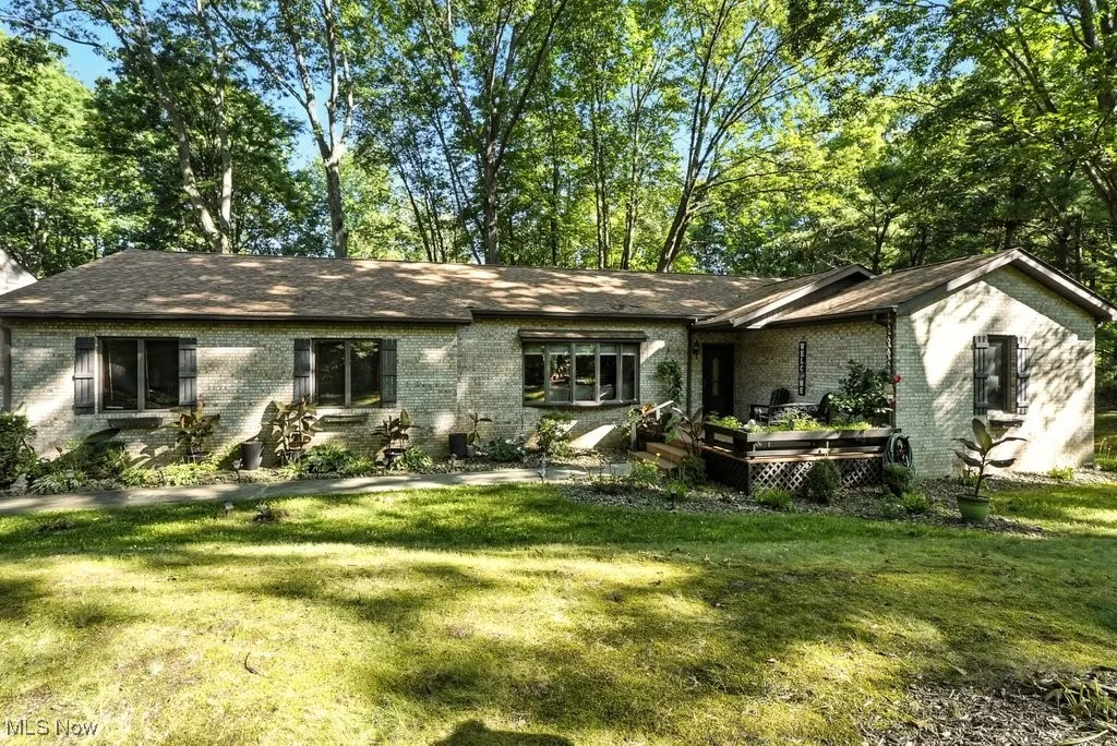 Ranch-style house with brick, a front yard, a wooden deck, and view of scattered trees