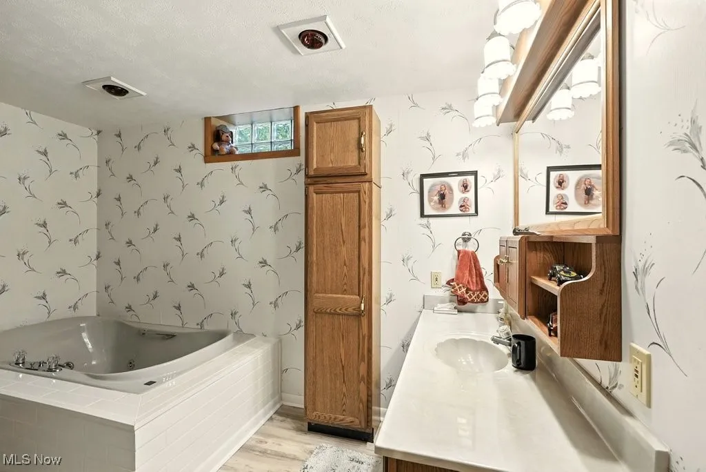 Bathroom with vanity, a whirlpool tub, wood finished floors, wallpapered walls, and a textured ceiling