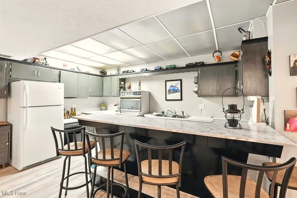 Kitchen with a peninsula, freestanding refrigerator, light countertops, light wood finished floors, and open shelves