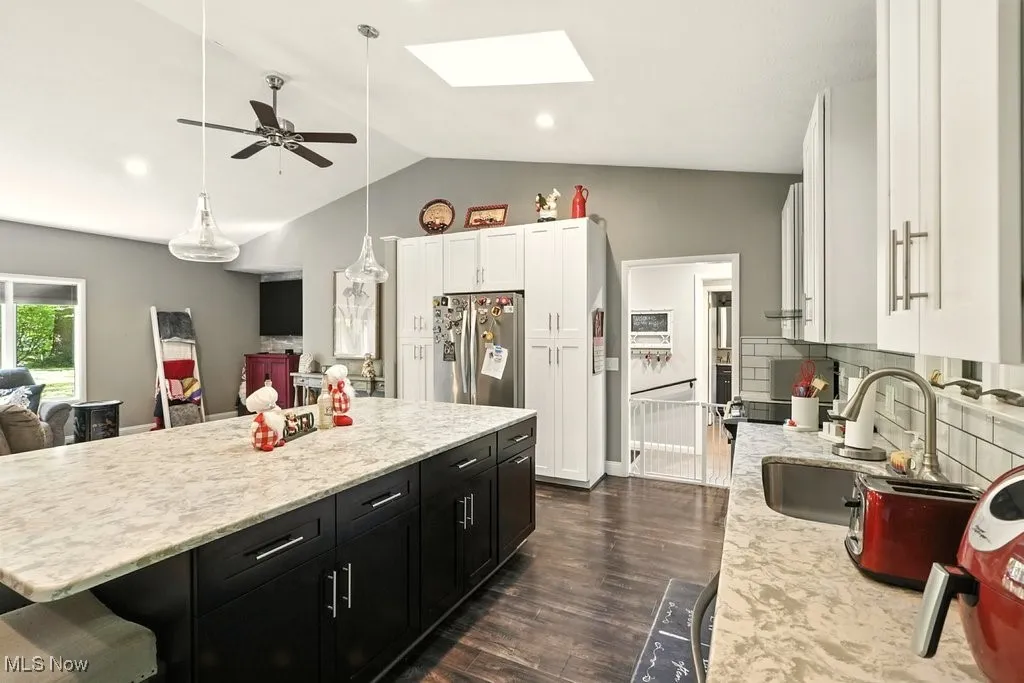 Kitchen featuring dark cabinets, freestanding refrigerator, ceiling fan, vaulted ceiling, and a kitchen island