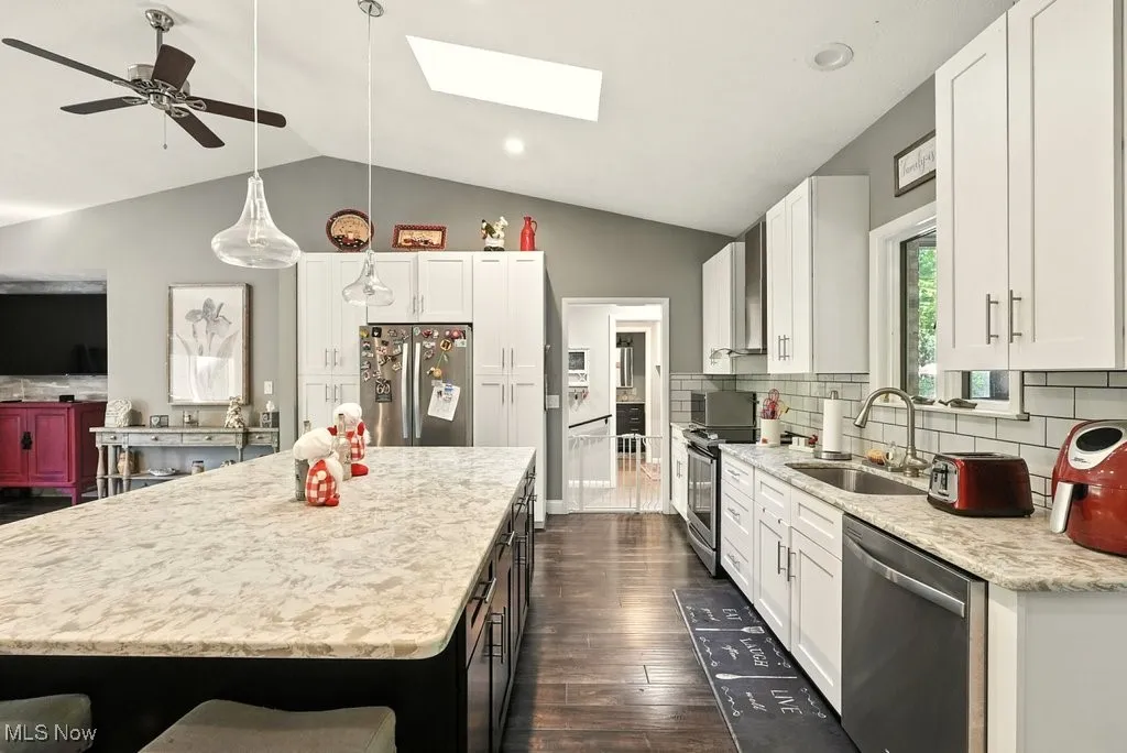 Kitchen featuring backsplash, stainless steel appliances, a center island, vaulted ceiling, and ceiling fan