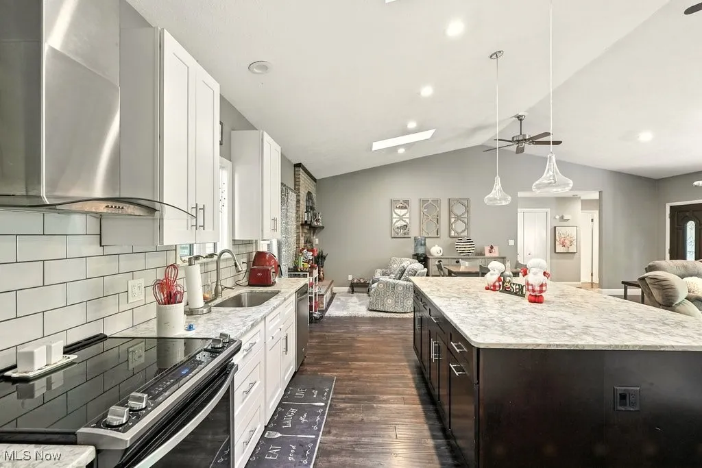 Kitchen featuring open floor plan, electric range, wall chimney range hood, lofted ceiling, and ceiling fan