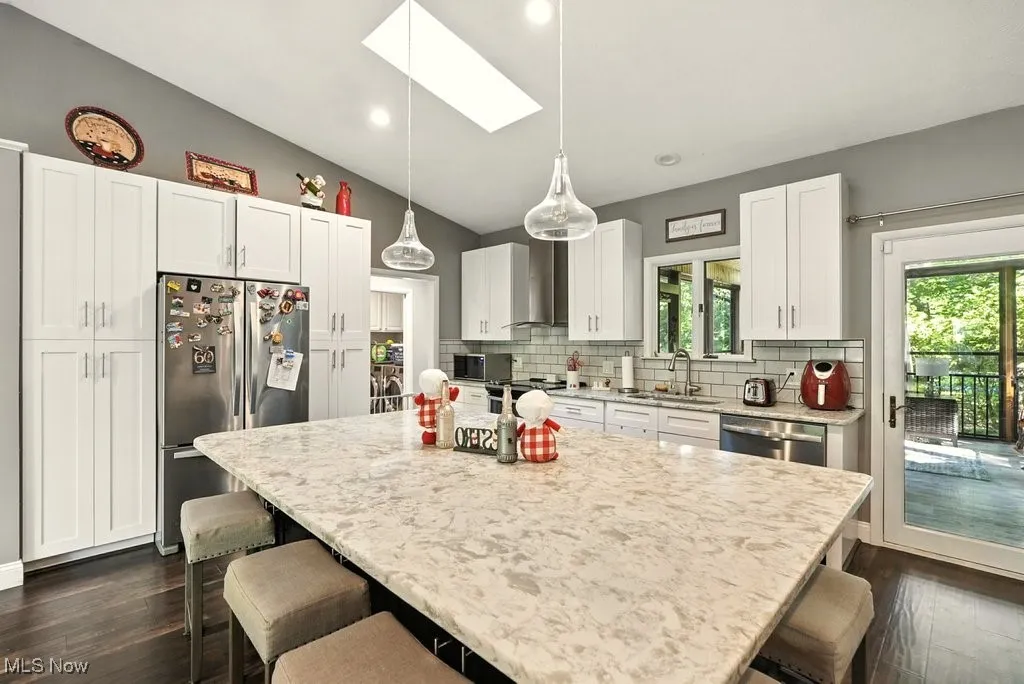 Kitchen with vaulted ceiling, a skylight, stainless steel appliances, dark wood-style floors, and a kitchen bar