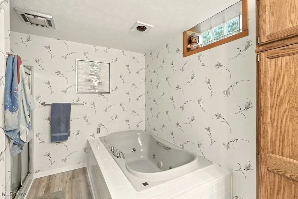 Full bath with a jetted tub, wood finished floors, and wallpapered walls