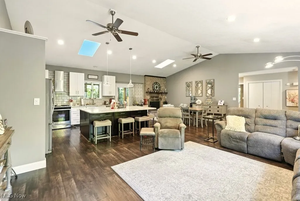 Living area with ceiling fan, vaulted ceiling, dark wood-style flooring, recessed lighting, and a skylight