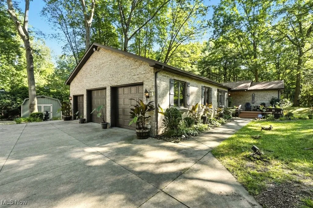 View of side of home featuring brick siding, concrete driveway, an outdoor structure, and view of scattered trees