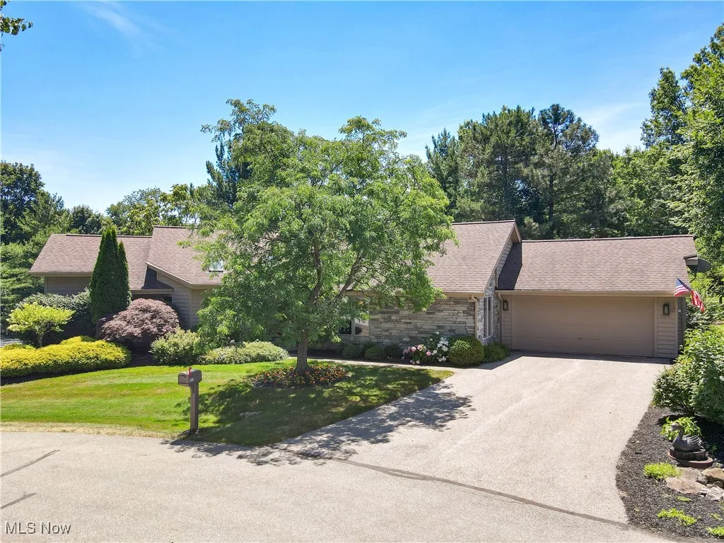 View of front of home featuring a garage, stone siding, driveway, a front lawn, and roof with shingles
