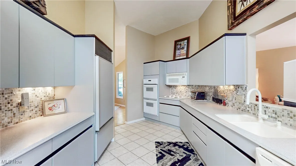 Kitchen featuring tasteful backsplash, white appliances, light tile patterned floors, and light countertops