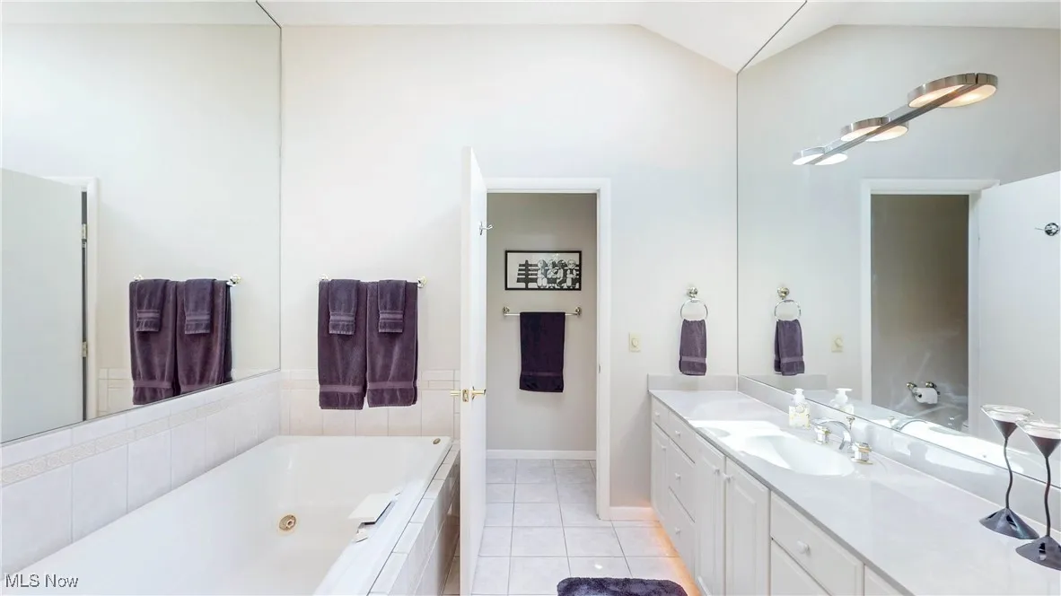 Bathroom with a whirlpool tub, vanity, tile patterned flooring, and vaulted ceiling