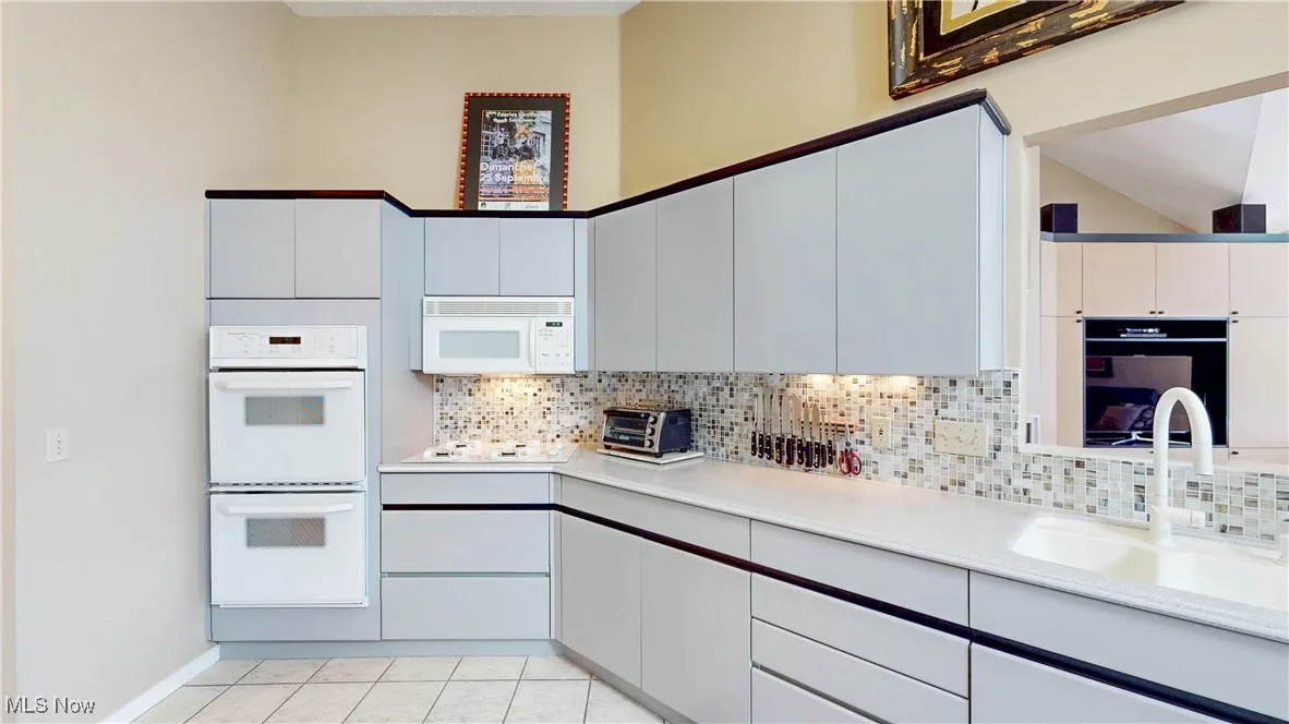 Kitchen with white appliances, light countertops, light tile patterned flooring, and tasteful backsplash