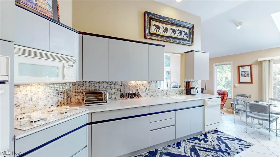 Kitchen featuring white appliances, light countertops, light tile patterned floors, and backsplash