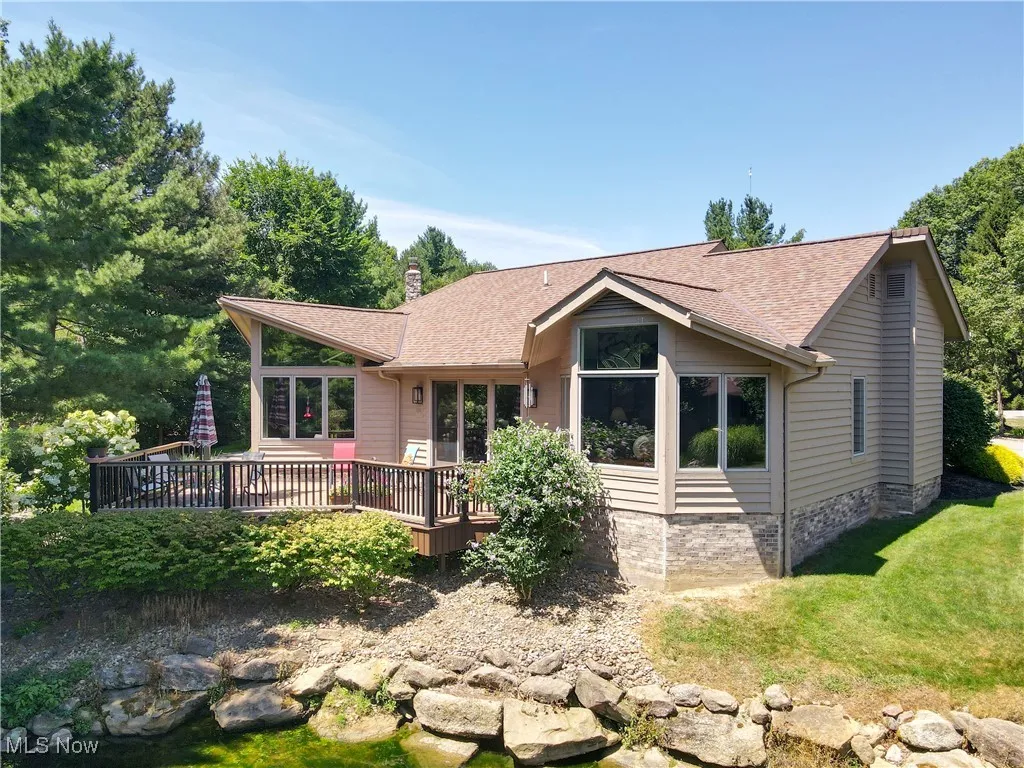 View of front of home with a wooden deck, a chimney, and a shingled roof