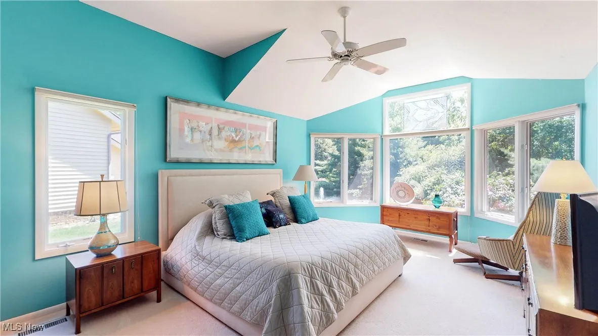 Bedroom with light carpet, multiple windows, vaulted ceiling, and a ceiling fan