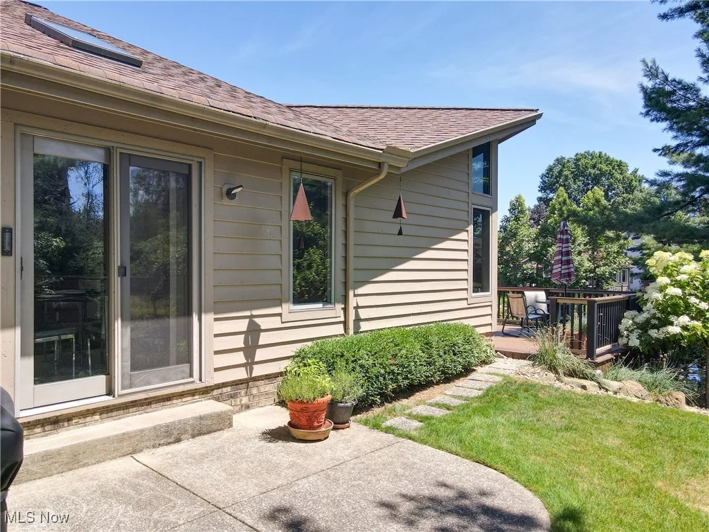 View of exterior entry with roof with shingles, a patio, and a yard