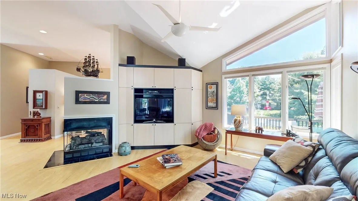 Living room featuring light wood-style floors, high vaulted ceiling, a fireplace with flush hearth, and a ceiling fan