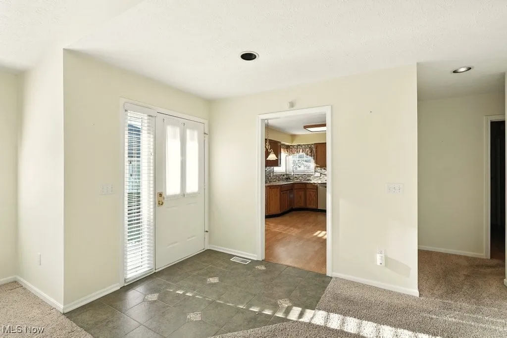 Entryway featuring a textured ceiling, dark colored carpet, and dark tile patterned floors