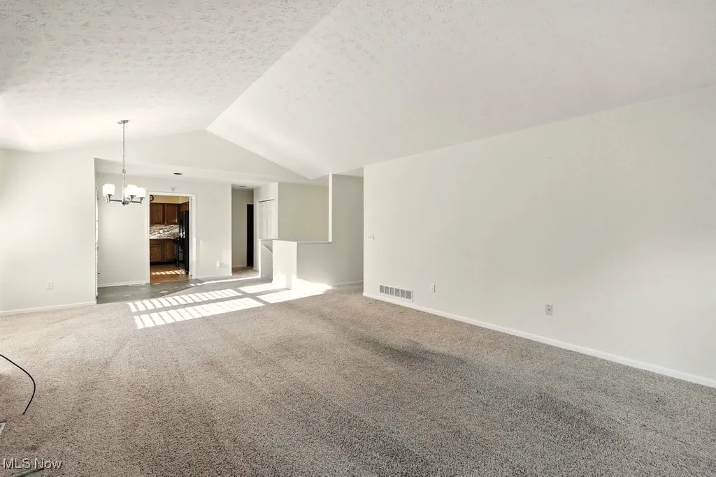 Unfurnished living room with carpet flooring, lofted ceiling, a chandelier, and a textured ceiling