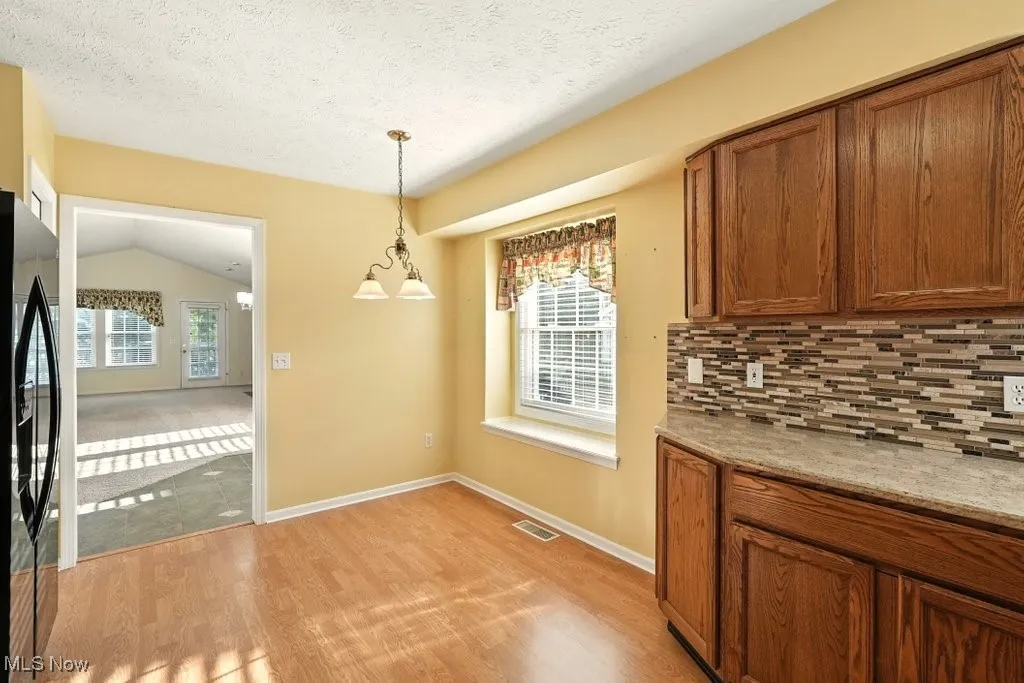 Unfurnished dining area featuring light wood-style floors, lofted ceiling, and a textured ceiling