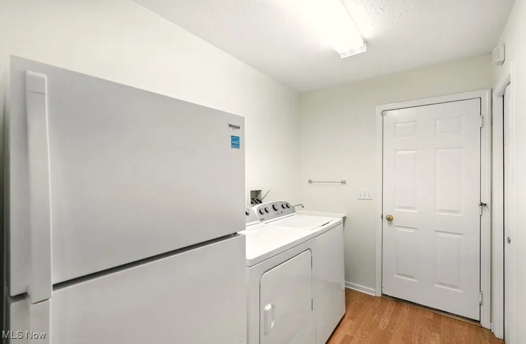Laundry area with washing machine and clothes dryer, light wood-style flooring, and a textured ceiling