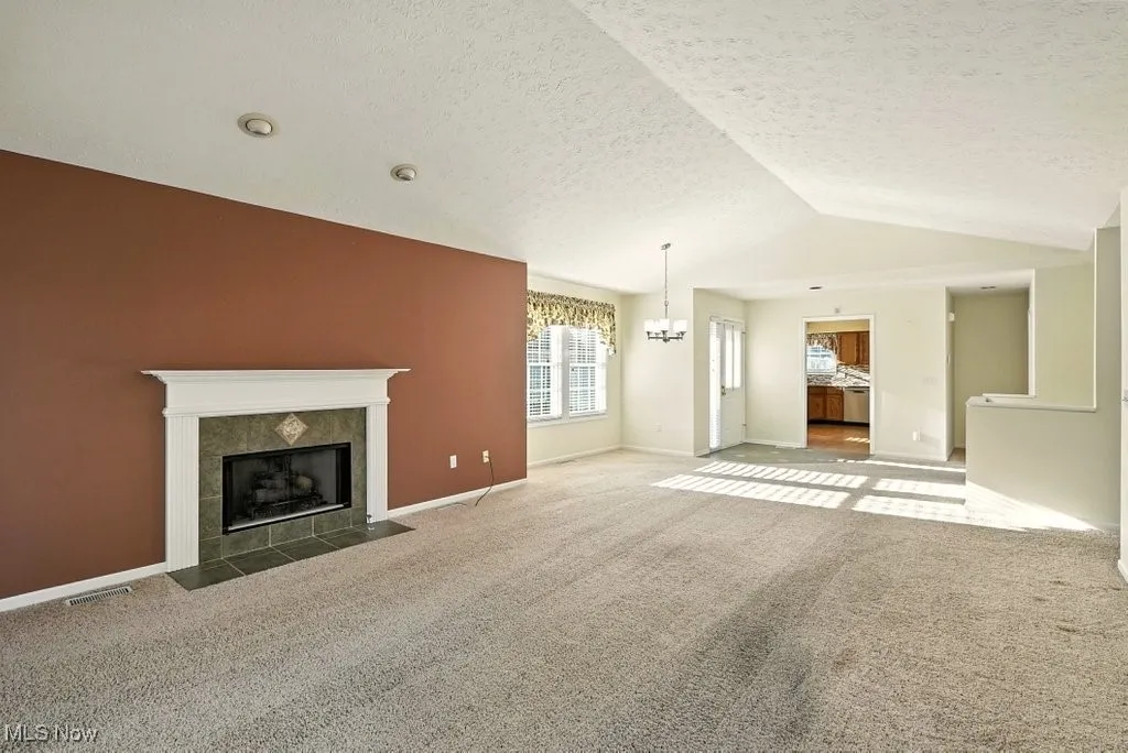 Unfurnished living room with vaulted ceiling, a tile fireplace, carpet floors, a textured ceiling, and a chandelier