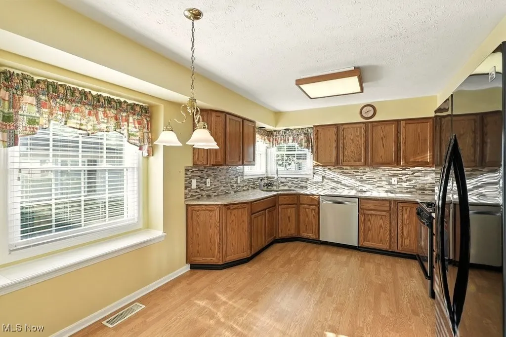 Kitchen featuring backsplash, brown cabinetry, black appliances, light countertops, and decorative light fixtures