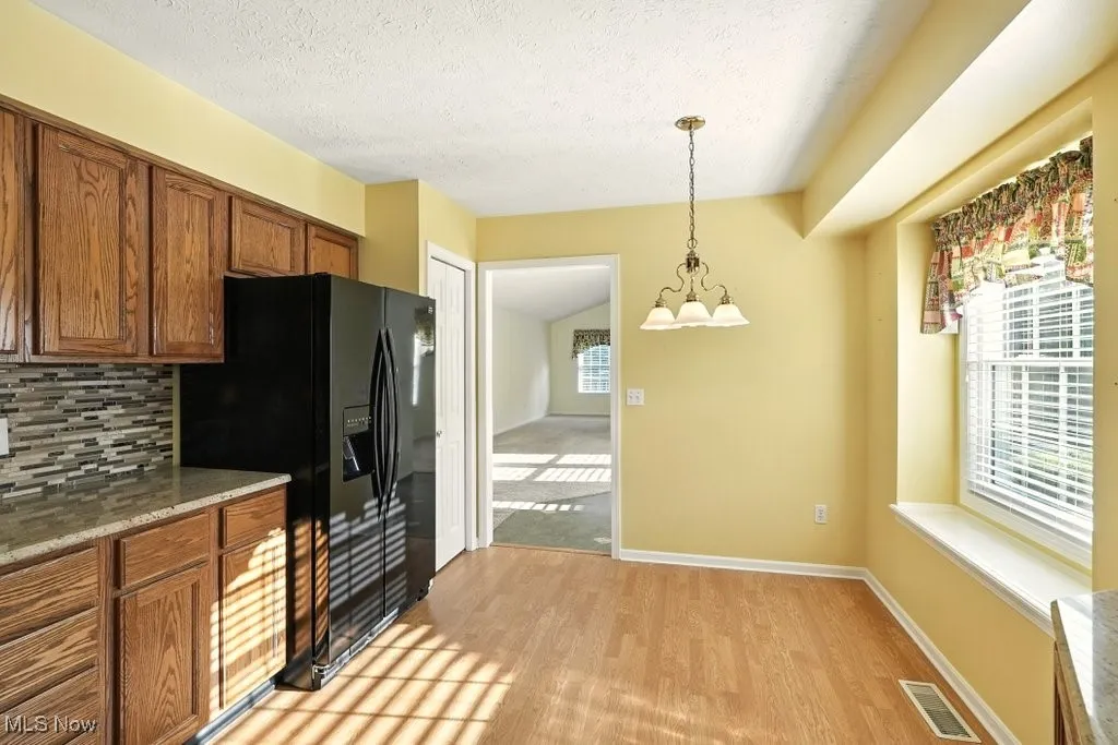Kitchen featuring backsplash, brown cabinetry, black refrigerator with ice dispenser, a chandelier, and hanging light fixtures