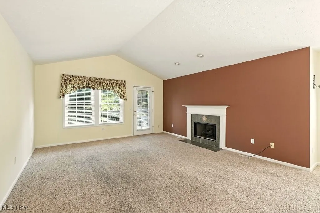 Unfurnished living room featuring carpet flooring, a tile fireplace, and lofted ceiling